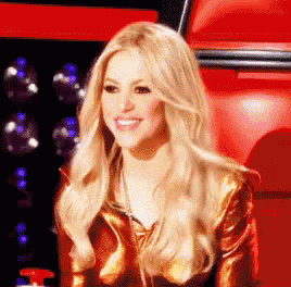 a woman with long blonde hair is smiling in front of a red wall