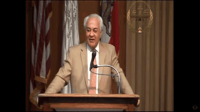a man in a suit and tie stands at a podium in front of a flag that says ' california ' on it