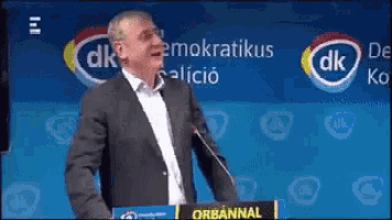 a man in a suit stands at a podium with a sign that says dk