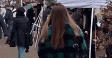 a woman in a green and black plaid shirt is walking down a street in front of a tent .
