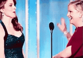 two women are standing in front of a microphone and laughing