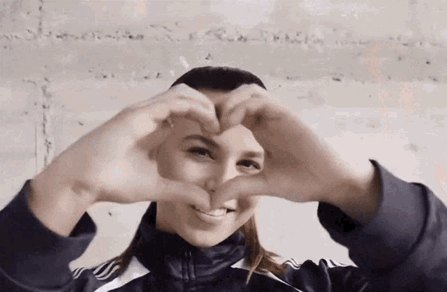 a woman making a heart shape with her hands in front of her face