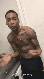 a shirtless man is standing in a bathroom with his hands in the air .