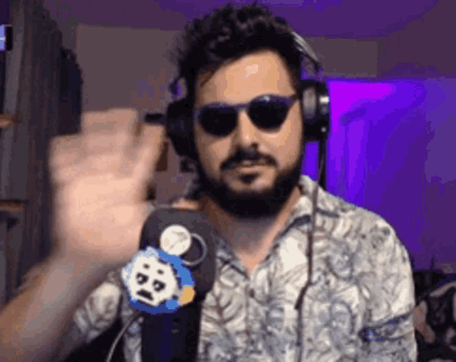a man with a beard wearing headphones and sunglasses is waving his hand .