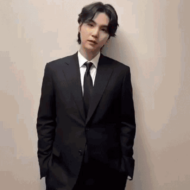a young man in a suit and tie is standing in front of a white wall .