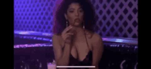 a woman in a very revealing black dress is smoking a cigarette in a bar .