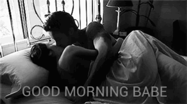a black and white photo of a man kissing a woman on a bed with the words good morning babe below them