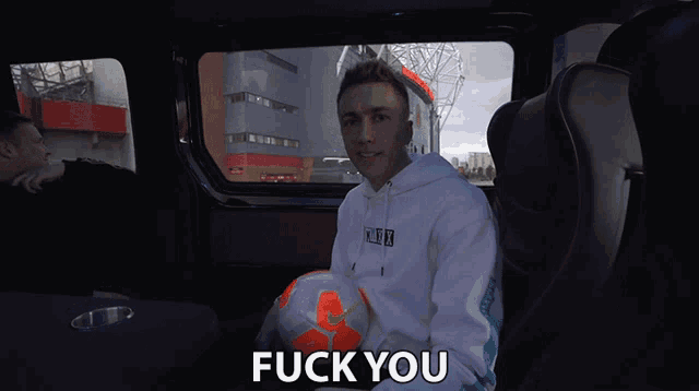 a man in a white hoodie is holding a soccer ball and the word fuck you is above him