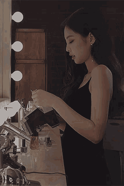 a woman in a black dress is standing in front of a mirror looking at something