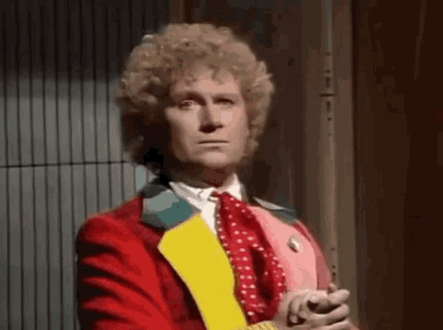 a man in a red suit and yellow tie is standing in front of a fence .