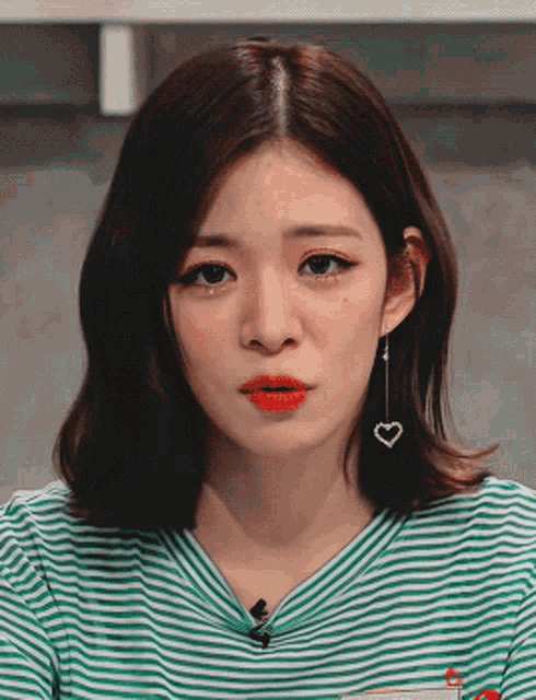 a woman wearing a green and white striped shirt has a heart shaped earring hanging from her ear