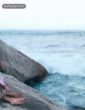 a person is sitting on a rock near the ocean with their feet in the water .