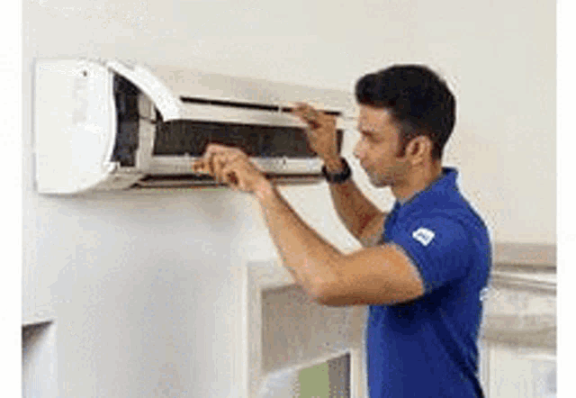 a man in a blue shirt is cleaning an air conditioner .
