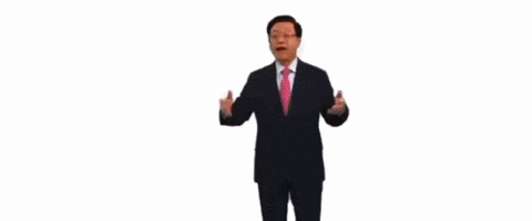 a man in a suit and pink tie is standing in front of a wall that says more on it