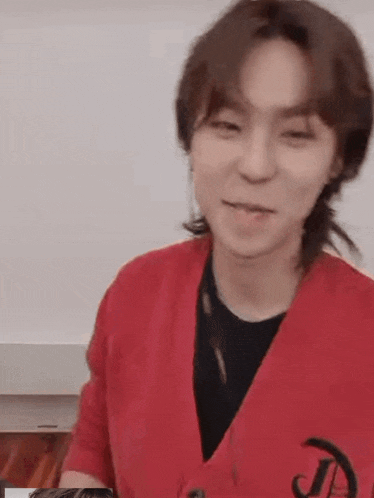 a man wearing a red cardigan and a black shirt is smiling .