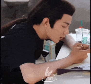 a man with a ponytail is sitting at a table looking at a cell phone