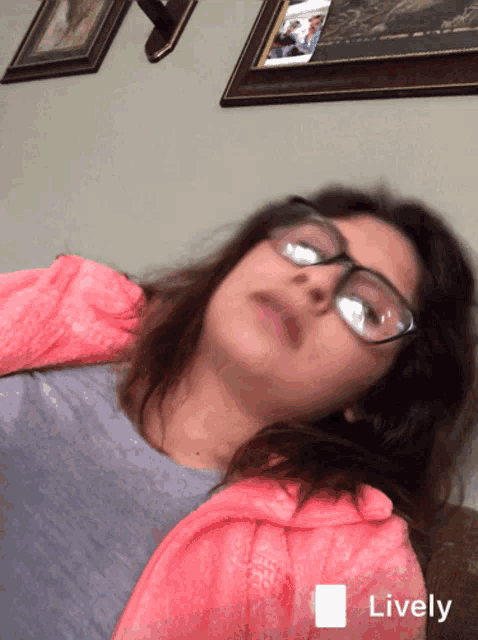 a girl wearing glasses and a pink jacket is laying on a couch and the word lively is on the bottom right