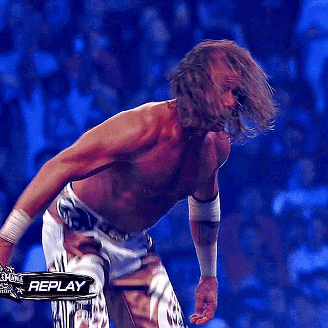 a shirtless wrestler stands in front of a replay banner