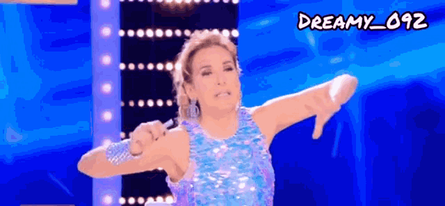 a woman in a blue sequined dress giving a thumbs down sign