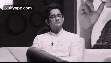 a man wearing glasses and a white shirt is sitting on a couch in a black and white photo .