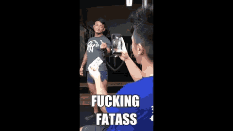 a man is taking a picture of another man in a gym with a caption that says fucking fatass .