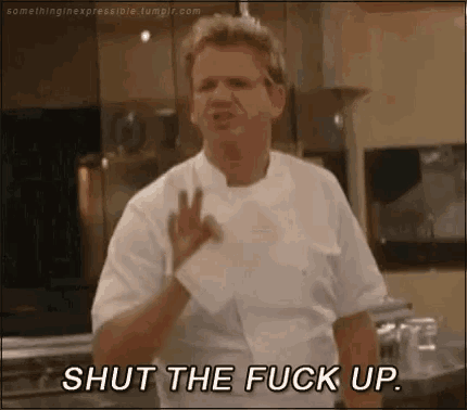 a man in a chef 's uniform is standing in a kitchen and giving the middle finger .
