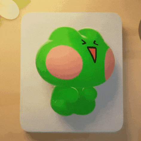 a green frog with a red beak is sitting on a table