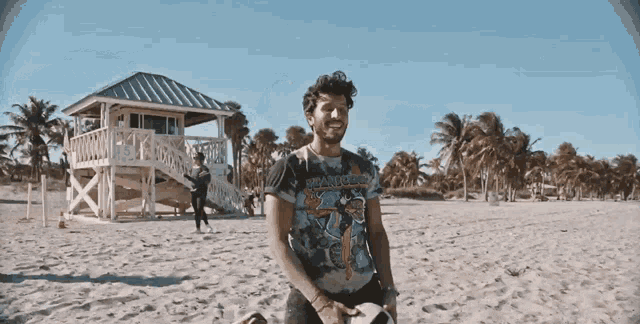 a man standing on a beach wearing a t-shirt that says iron maiden on it
