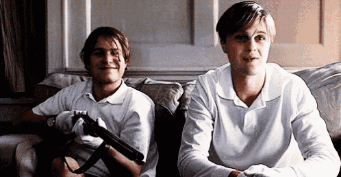 two young men are sitting on a couch holding guns and smiling .