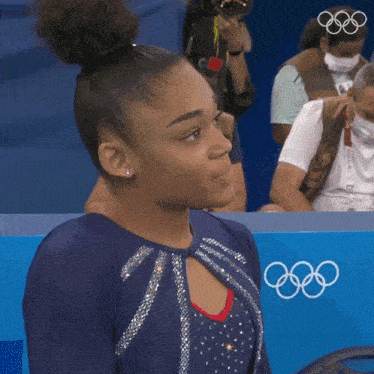 a female gymnast stands in front of a sign that says olympics