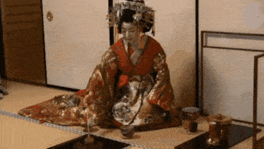 a woman in a kimono is sitting on the floor with a cup in her hand