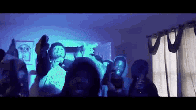 a group of people are dancing in a living room in front of a blue light .
