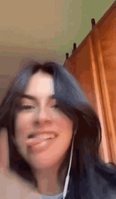 a woman with blue hair is smiling and sticking her tongue out while wearing headphones .