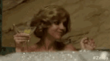 a woman is taking a bath in a bathtub while holding a glass of champagne .
