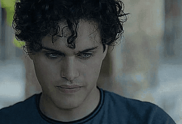 a young man with curly hair is wearing a blue shirt and looking at the camera .