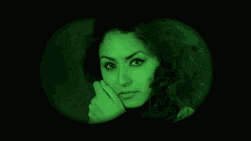 a woman 's face is visible through a binoculars in a green light .