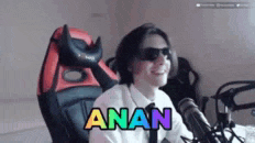 a man wearing sunglasses and a tie is sitting in front of a microphone with the word anan written on his face .