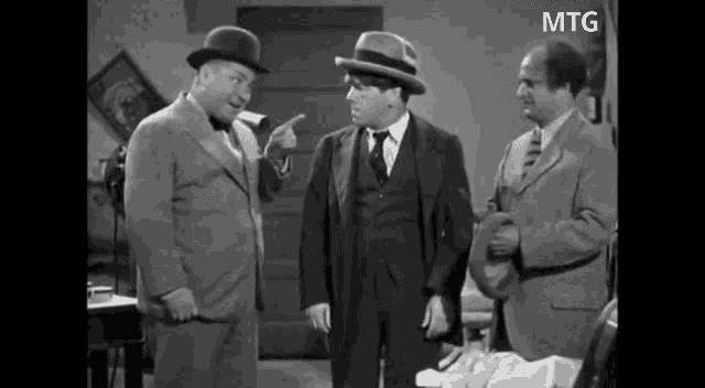 three men in suits and hats are standing next to each other and talking in a room .