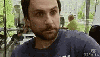 a man with a beard is sitting at a table in a restaurant making a funny face .