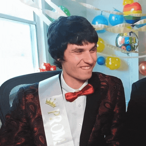 a man wearing a sash that says prom is smiling