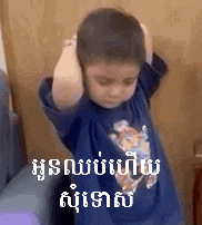 a young boy is covering his ears with his hands while standing in a room .