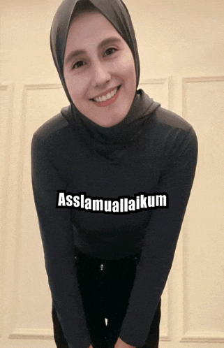 a woman wearing a hijab and a black shirt with the words assalamualaikum written on it
