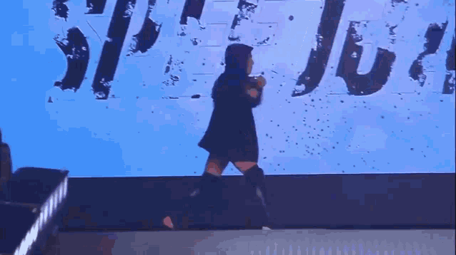a woman is walking on a stage with a microphone in front of a screen that says ' a ' on it .