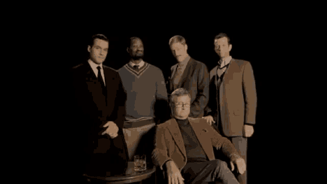 a group of men are posing for a picture with one man sitting in front of a glass of whiskey