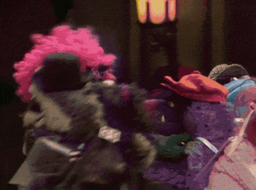 a clown with a pink wig and a top hat stands next to a purple clown