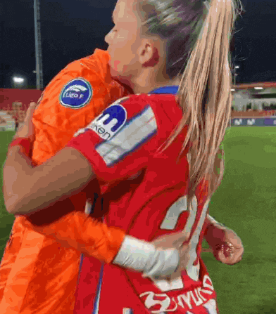 two female soccer players are hugging each other on a field and one of the players has the number 21 on her back