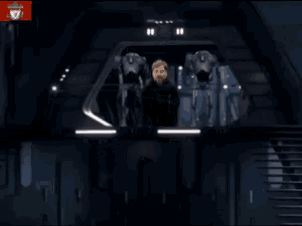 a man with a beard is standing in a room with a robot in the background