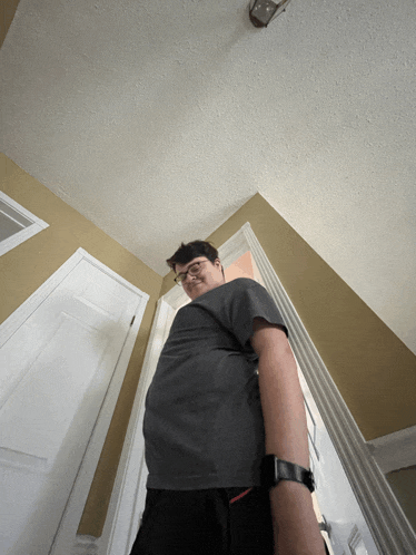 a man wearing glasses and a watch stands in a hallway looking up at the ceiling