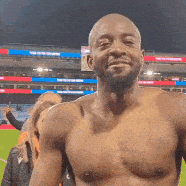 a man without a shirt is standing on a field with a woman taking a picture of him .