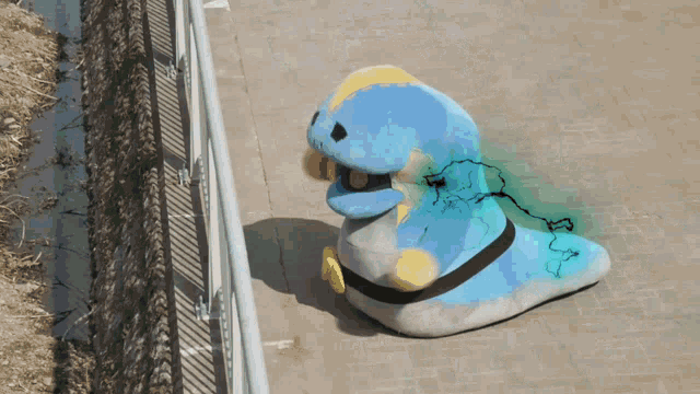 a blue and white stuffed animal is sitting on the sidewalk next to a fence